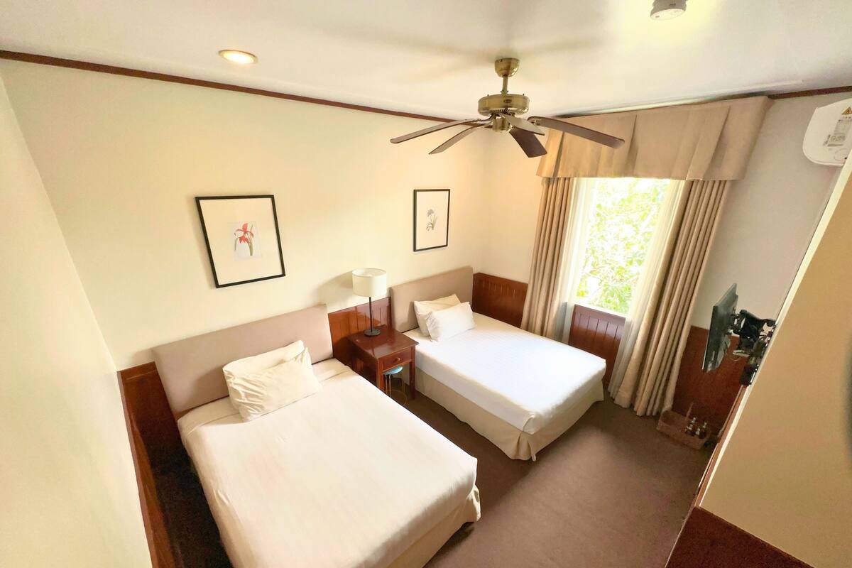 A hotel room with two beds, a ceiling fan, and a window with curtains.