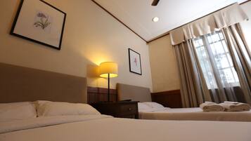 A hotel room with two beds, a nightstand with a lamp, and a window with curtains.