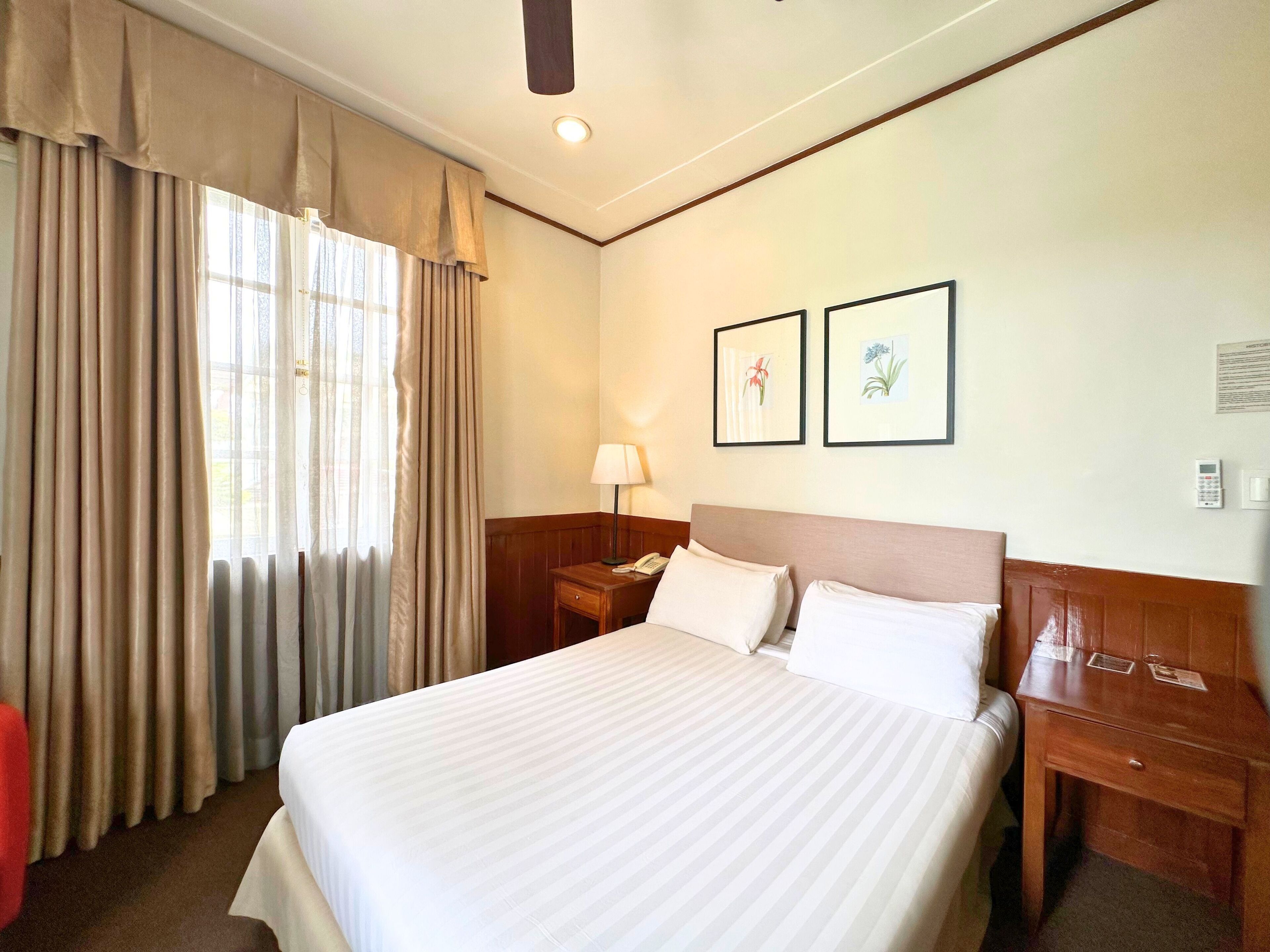 A hotel room with a large bed, a nightstand, a lamp, and two framed pictures on the wall.