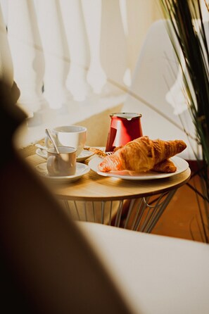 A table with a croissant, a cup, and a red can, likely containing a beverage. - Room Chueca (Madrid)