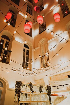 A multi-level interior with string lights and red lanterns, a balcony with a railing, and shelves with glass bottles.
