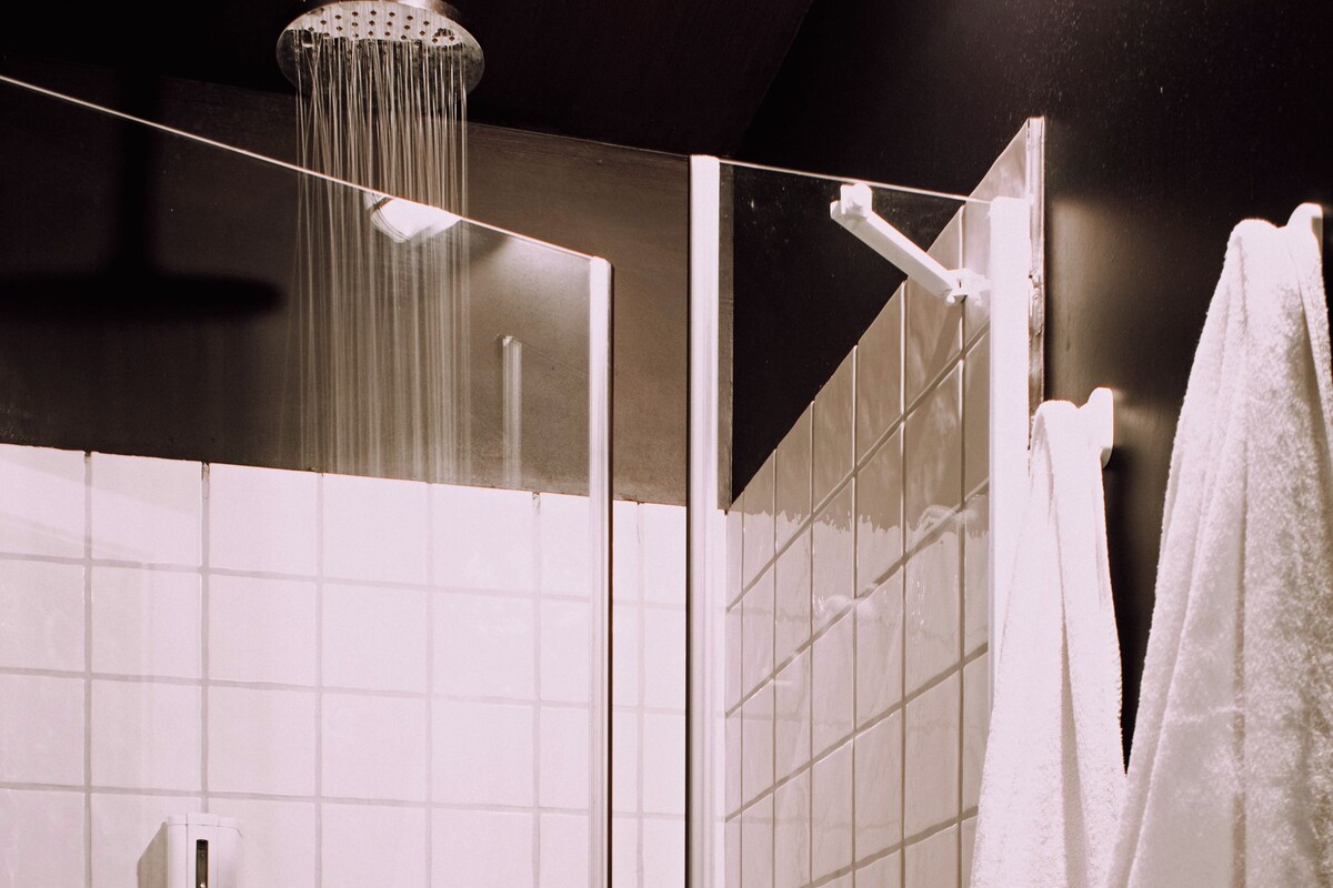 Une douche équipée d’un pommeau de douche à effet pluie, d’un distributeur de savon et d’un porte-serviettes avec des serviettes.
