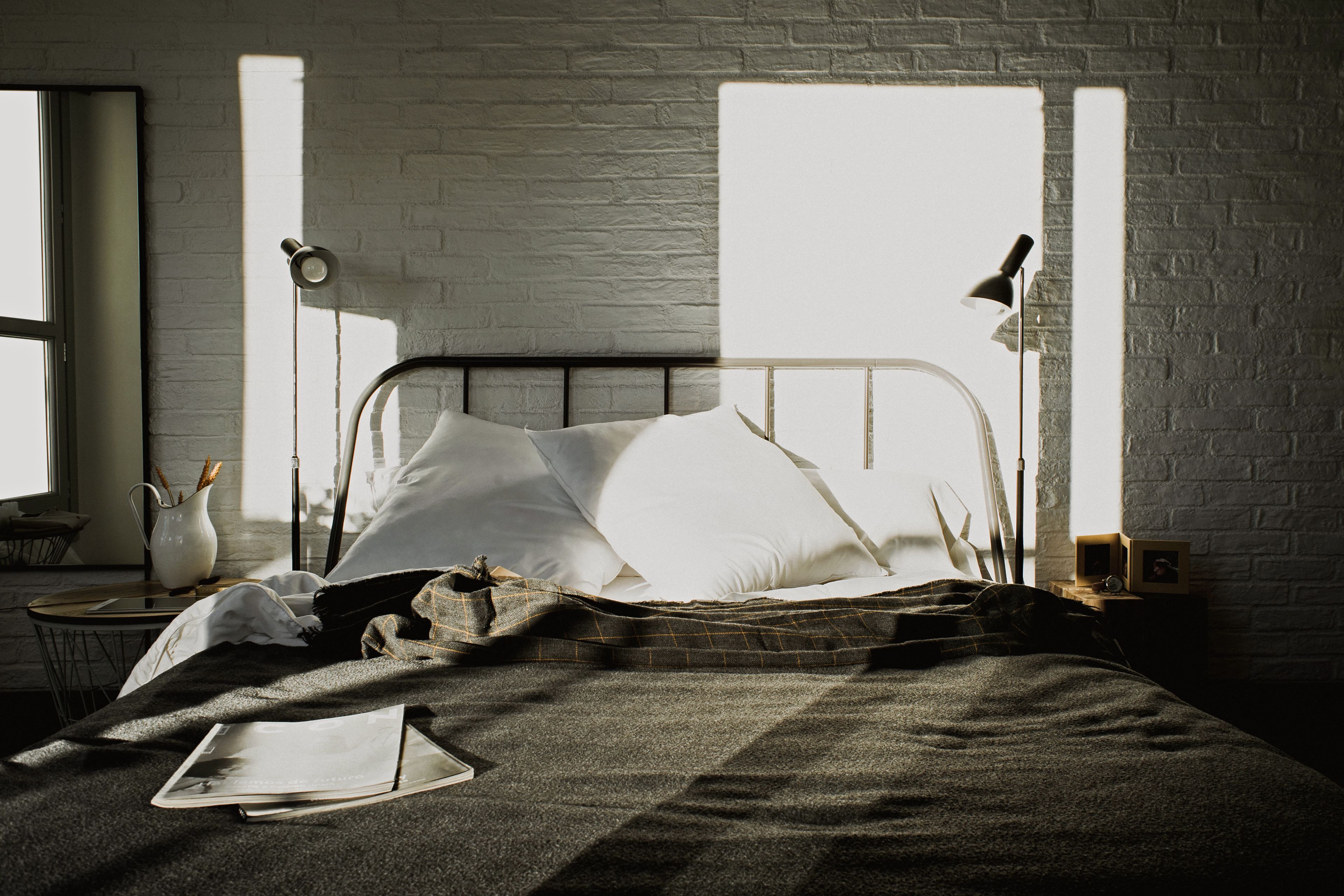 A neatly made bed with a checkered blanket, a bedside table with a lamp, and a window with natural light.