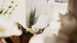 A room with a view of a cityscape through a window, a white chair, a small table with a cup, and a potted plant. - Room Chueca (Madrid)