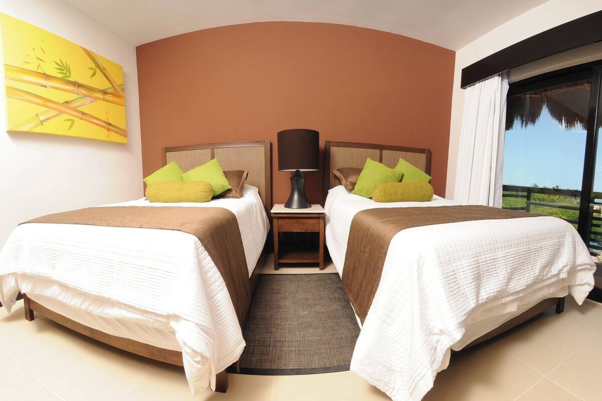 Une chambre d’hôtel avec deux lits, une table de chevet, une lampe, une grande fenêtre et un tableau au mur.