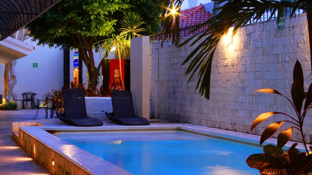 A swimming pool with lounge chairs, surrounded by stone walls and plants, under evening lighting.