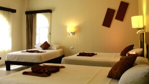 A hotel room with two beds, each with a pillow and a blanket. There is a wall-mounted lamp and a window with curtains.