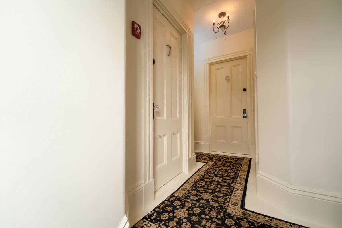 A hallway with white doors, a black and beige patterned carpet, and a wall-mounted light fixture.