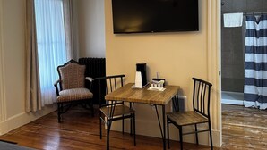 A room with a wooden table, two chairs, a TV on the wall, a radiator, and a window with curtains. - The Whitetail and Suites (Lincoln)