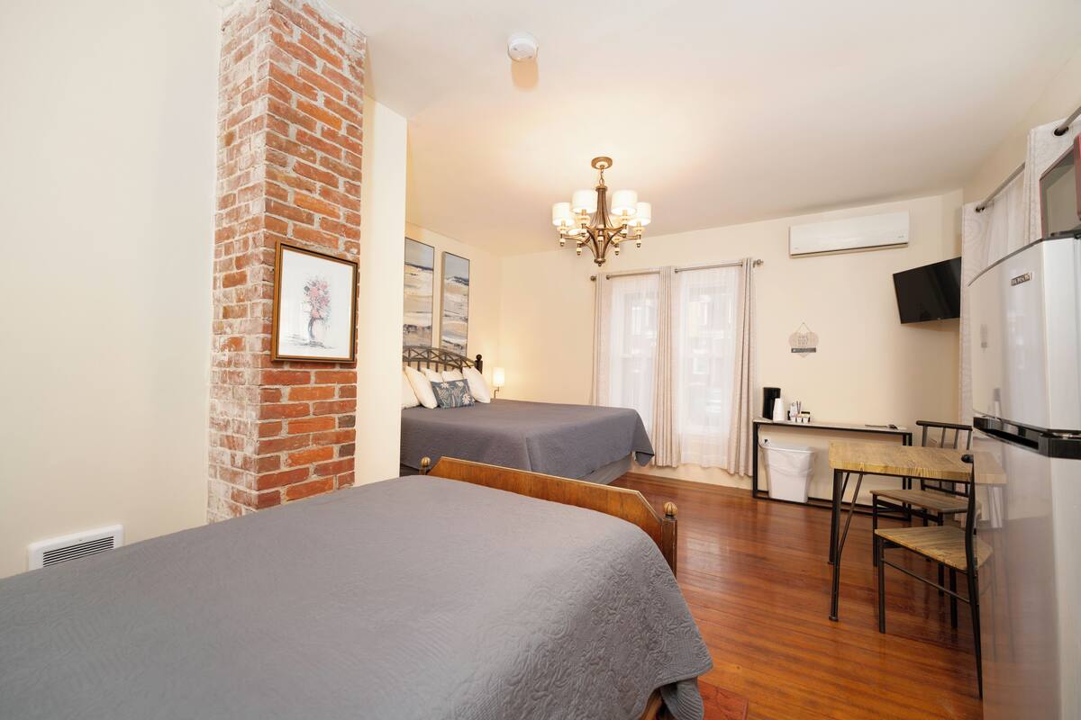 A hotel room with two beds, a dining table, a TV, and a refrigerator.
