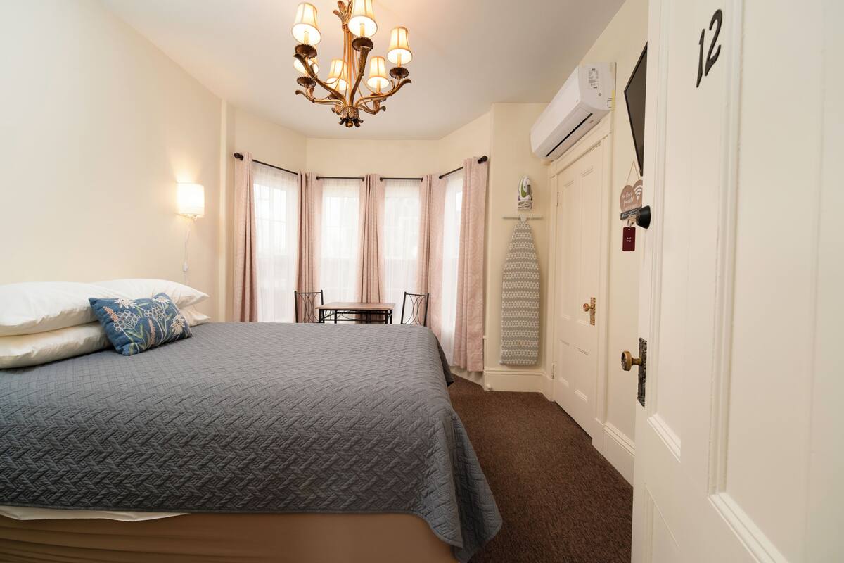 A bedroom with a bed, a chandelier, a desk, and a door.