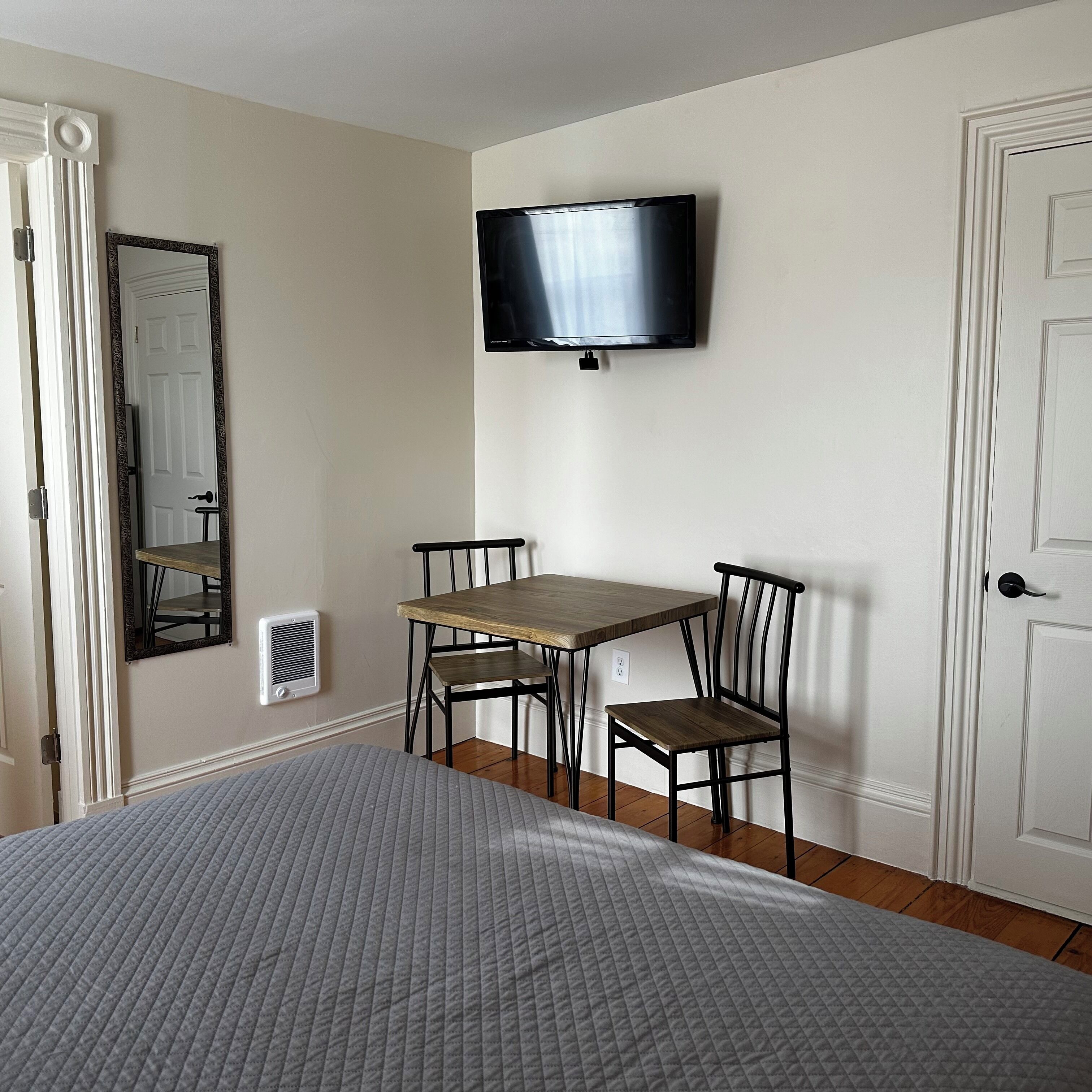 Une pièce comprenant un lit, une table avec deux chaises, un téléviseur fixé au mur et une porte.