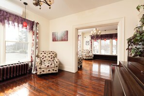 A room with wooden flooring, a radiator, a patterned armchair, and a view through an open doorway.