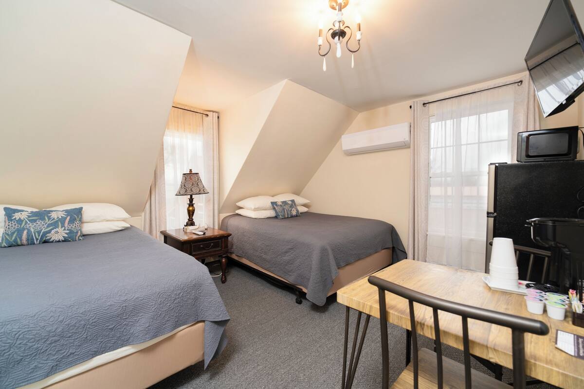 A bedroom with two beds, a desk, a television, and a window with curtains.