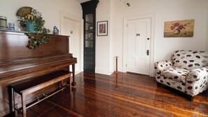 A room with a wooden piano, a patterned armchair, and a door with numbers 12 and 26. - The Whitetail and Suites (Lincoln)