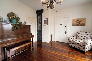 Um quarto com um piano de madeira, uma poltrona estampada e uma porta com os números 12 e 26.