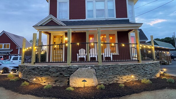 A two-story house with a porch, stone foundation, and string lights. - The Whitetail and Suites (Lincoln)