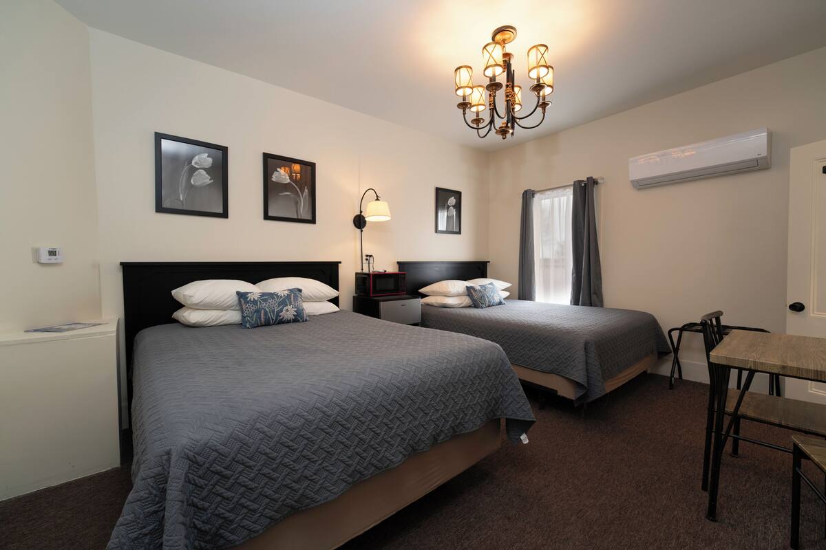 A hotel room with two beds, a desk, a chair, a chandelier, and framed pictures on the wall.