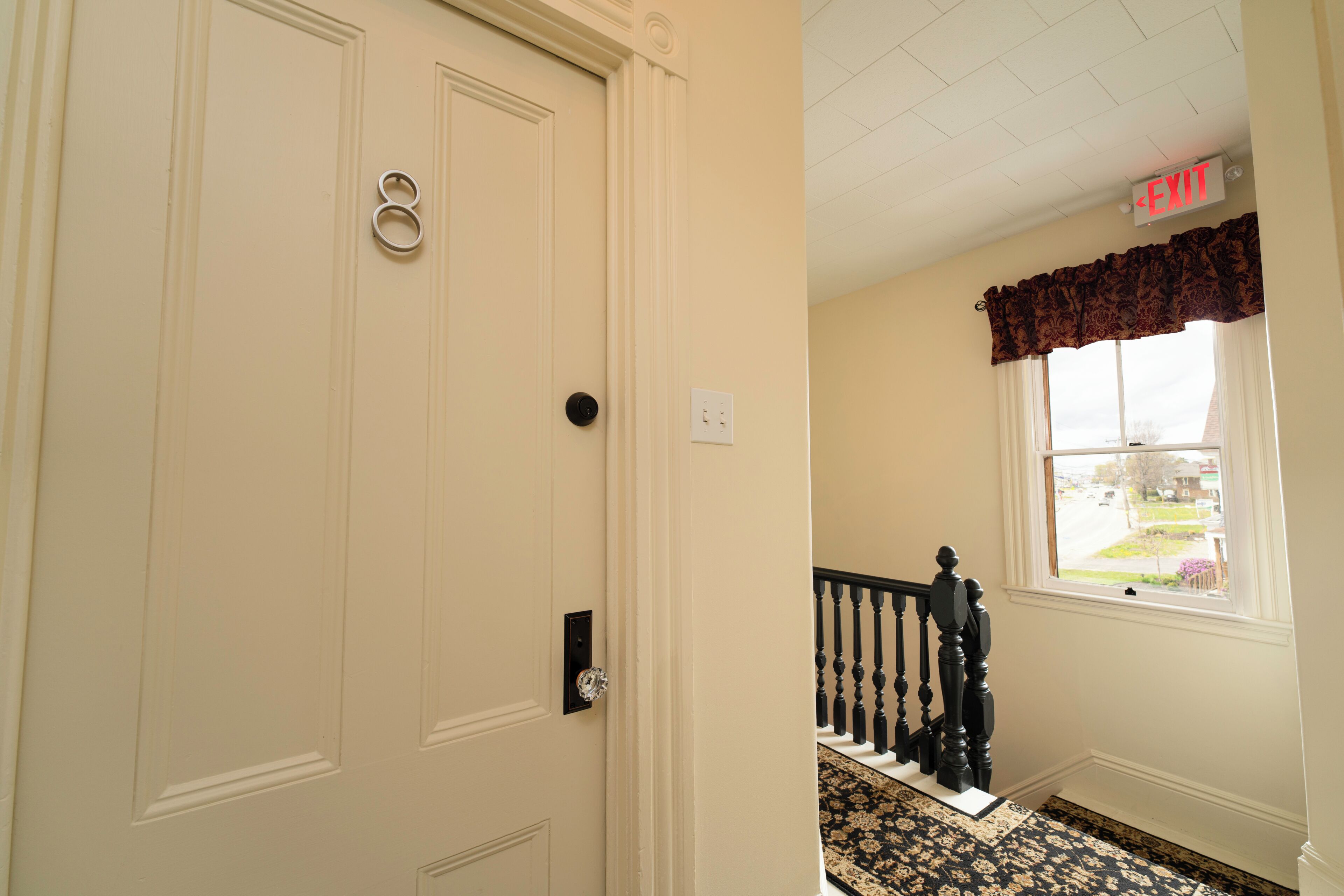 A door with a number, a staircase with a railing, and a window with a view of the outside.