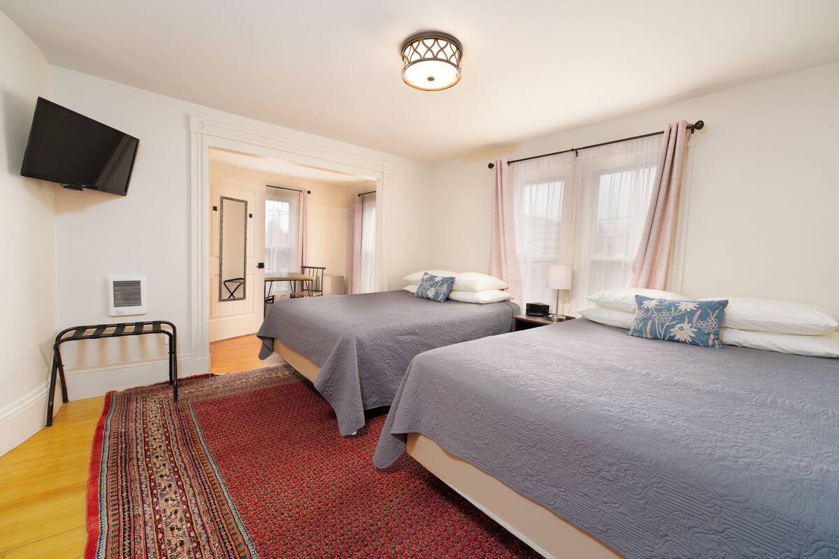 A hotel room with two beds, a television, a mirror, and a red patterned rug.