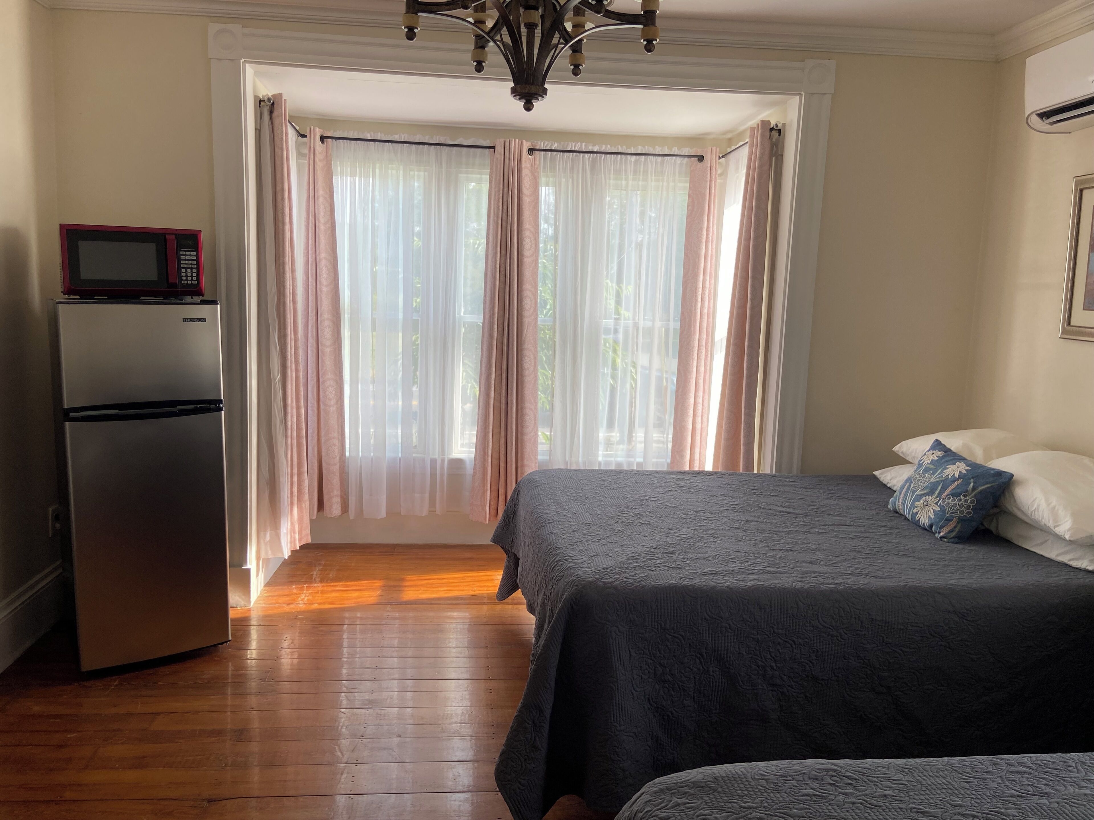 Un dormitorio con cama, mesita de noche, refrigerador y ventana con cortinas.
