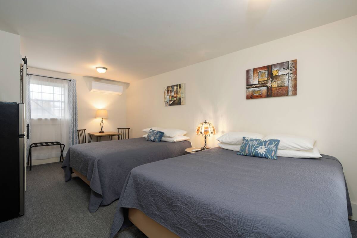 A hotel room with two beds, a desk, a chair, a lamp, and artwork on the walls.