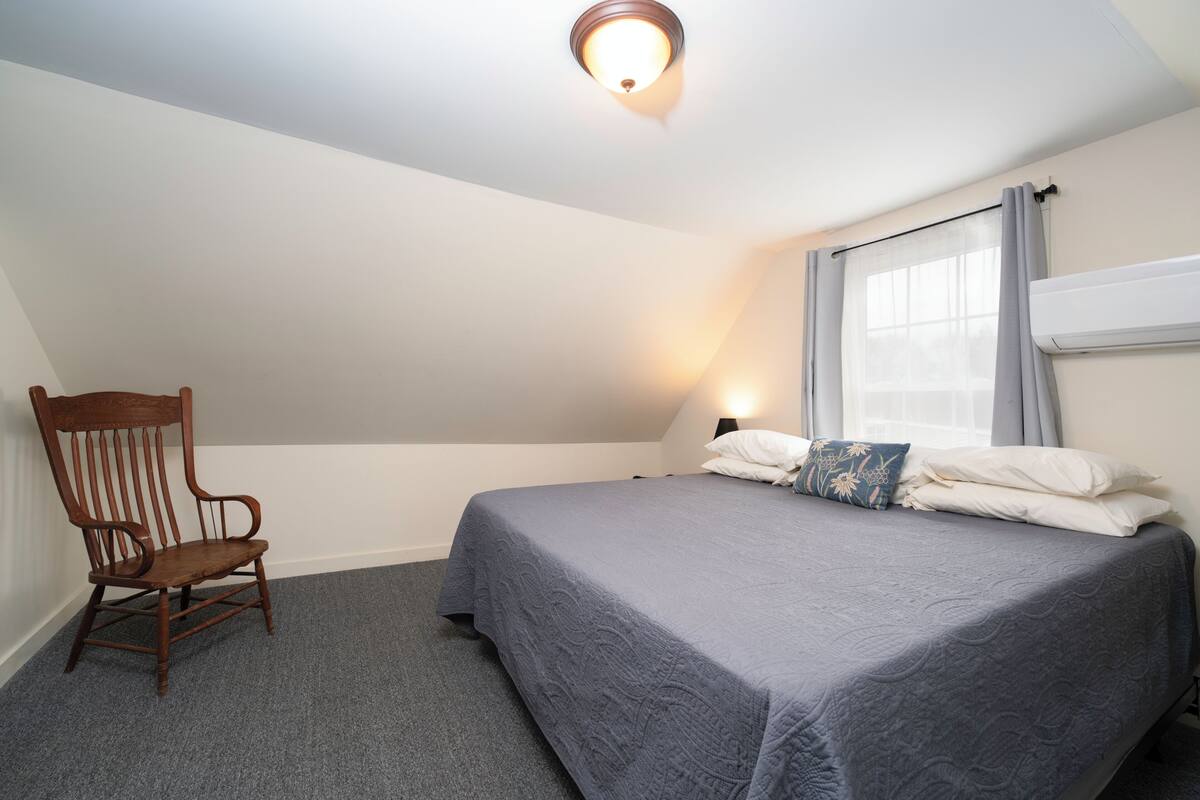 A bedroom with a bed, a chair, a window with curtains, and a ceiling light fixture.
