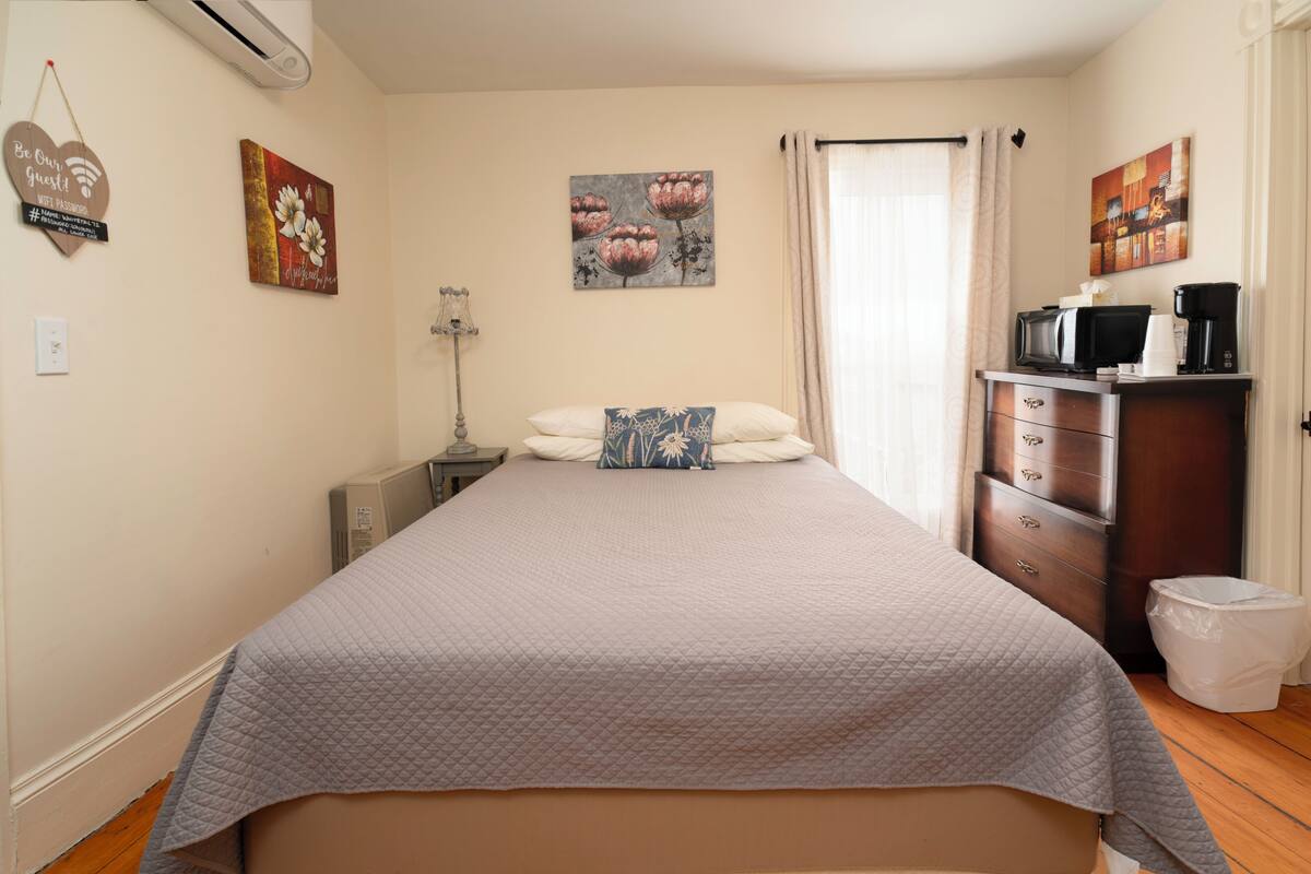 A bedroom with a bed, a dresser, a trash bin, and wall art.