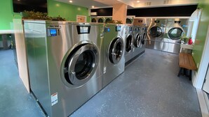 A row of modern, stainless steel front-loading washers in a commercial setting. - The Whitetail and Suites (Lincoln)