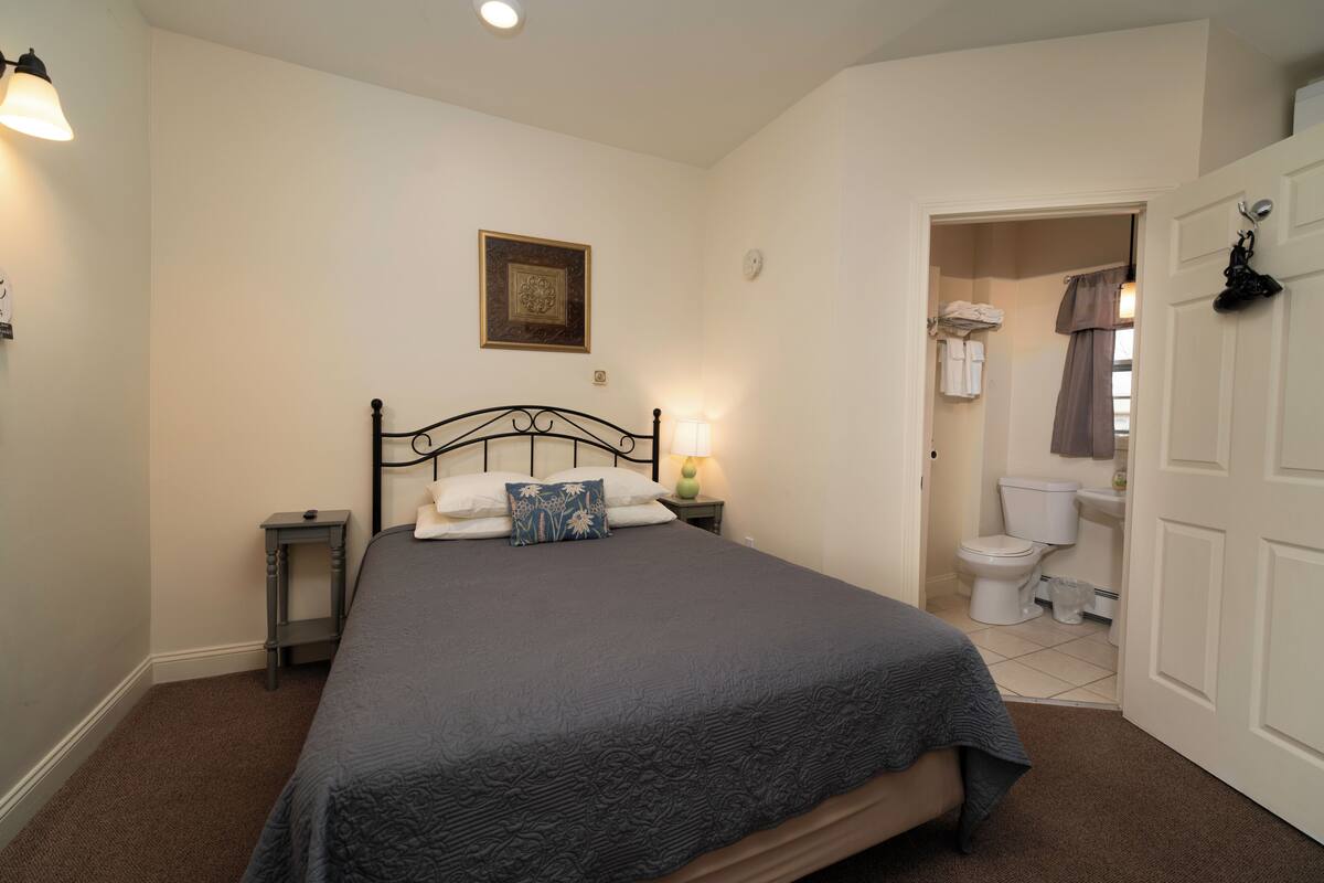 A bedroom with a bed, bedside lamp, and a door leading to a bathroom.
