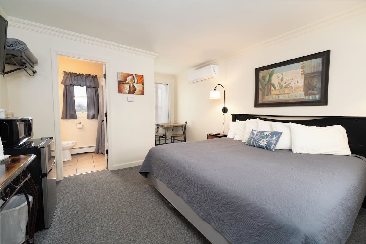 A hotel room with a bed, a desk, a chair, a TV, and an air conditioning unit.