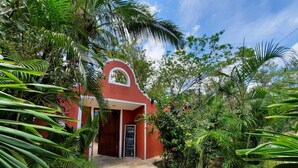 A red building with a curved entrance, surrounded by lush tropical vegetation. - Casa Don Diego (Tulum)