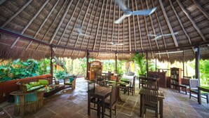 A covered outdoor seating area with wooden furniture and a thatched roof. - Casa Don Diego (Tulum)