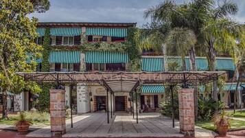A hotel with a covered entrance, stone pillars, and a garden with palm trees.