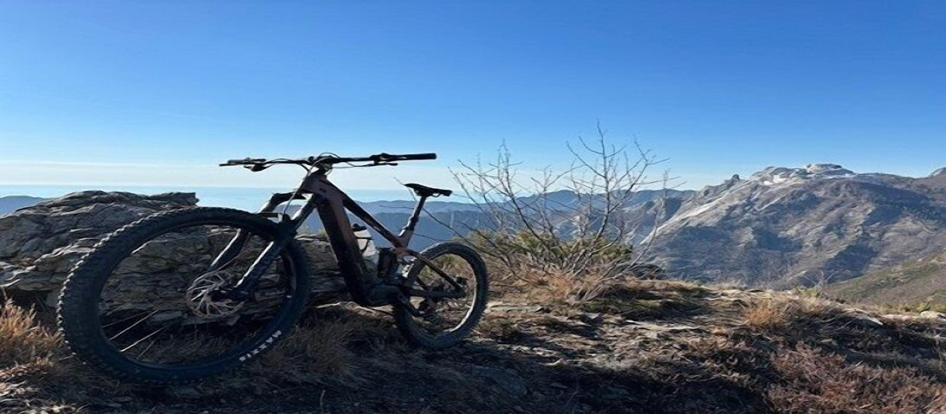 Una mountain bike parcheggiata su terreno roccioso con una vista aperta sulle montagne lontane.