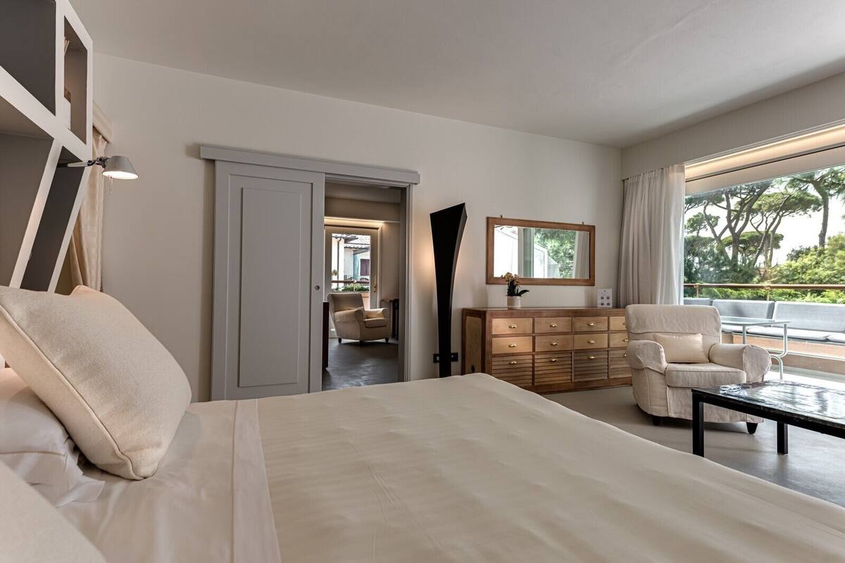 Une chambre à coucher moderne avec un grand lit, une commode, un fauteuil et une vue sur l’extérieur.