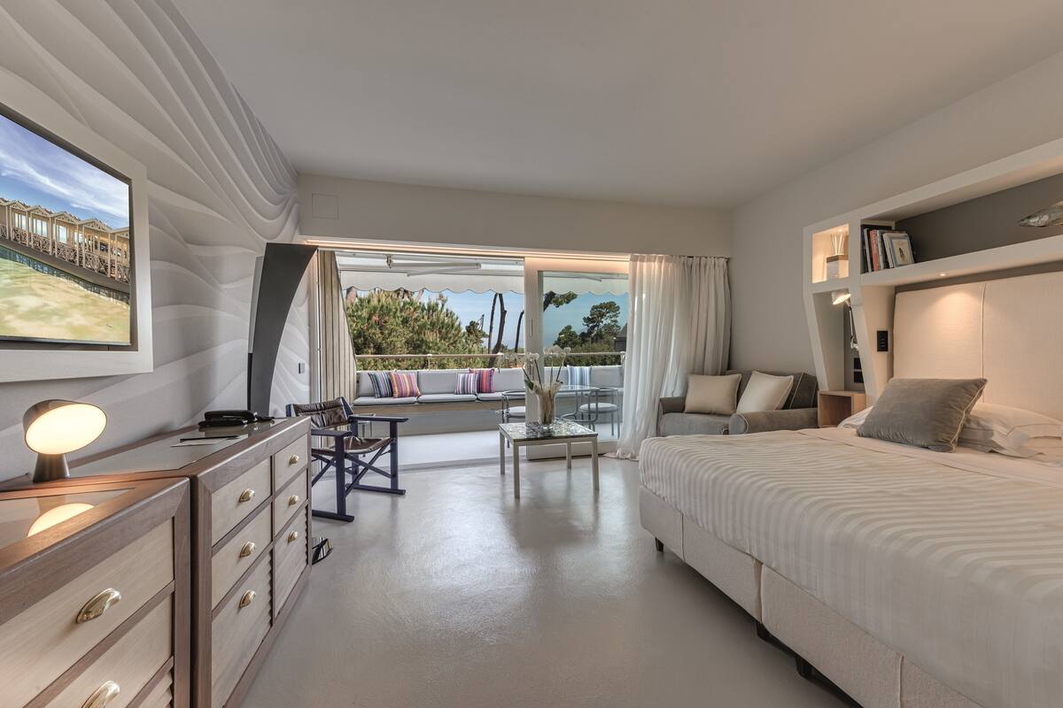 Une chambre d’hôtel moderne, dotée d’un grand lit, d’un bureau avec une lampe, d’un canapé et offrant une vue sur l’extérieur.
