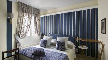 A bedroom with a bed, pillows, a chair, a bedside table, a lamp, and a window with curtains.