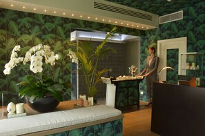 A reception area with a modern design, featuring a reception desk, a large potted plant, and a seating area with a cushioned bench. - Augustus Hotel & Resort (Forte dei Marmi)