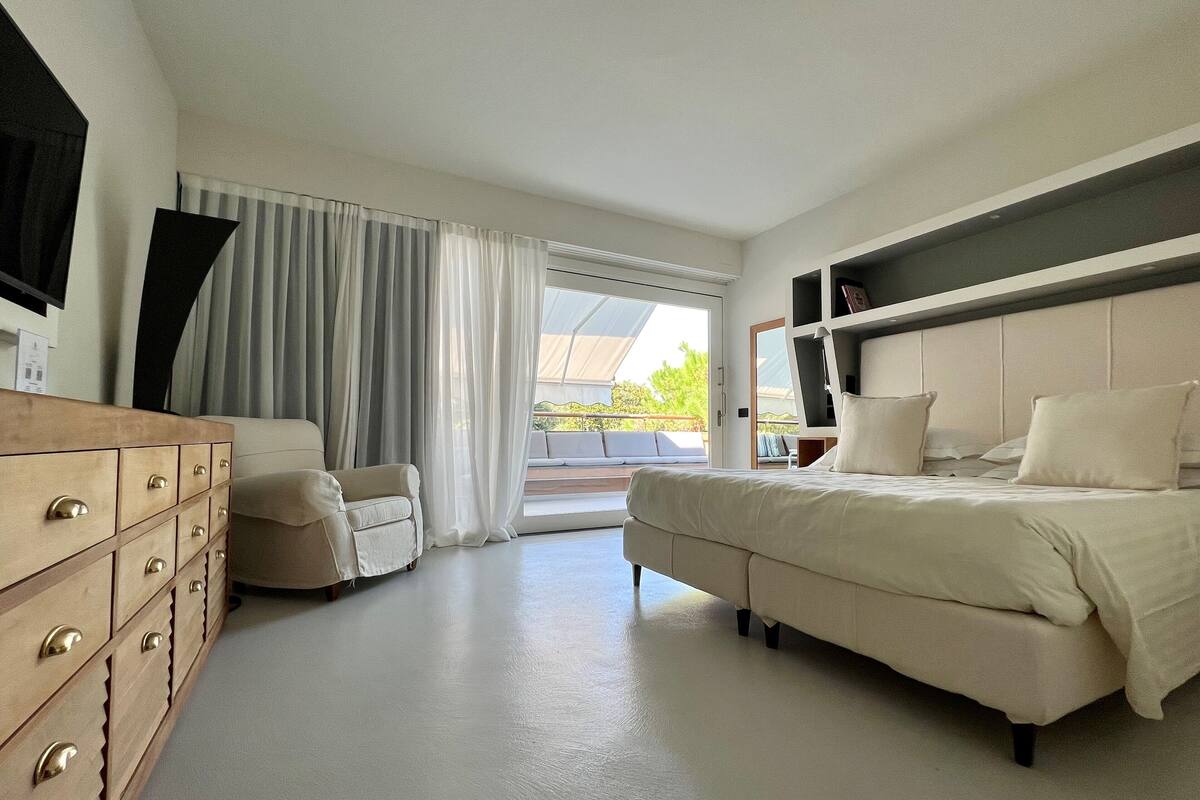 Une chambre d’hôtel moderne avec un grand lit, un canapé, une commode en bois et un téléviseur fixé au mur.