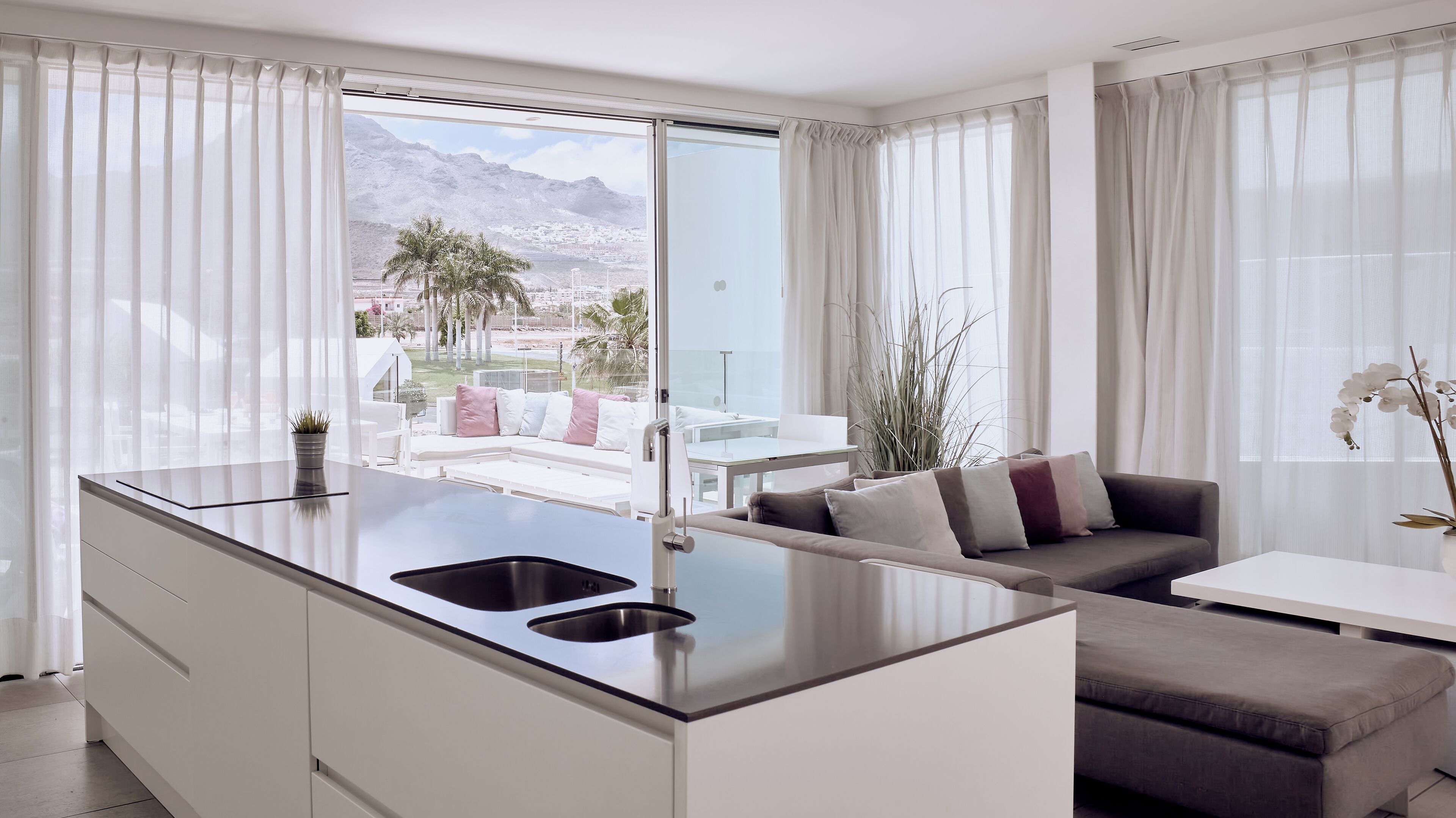 A modern kitchen with a central island, a dining area with a white table and chairs, and a sofa with cushions.