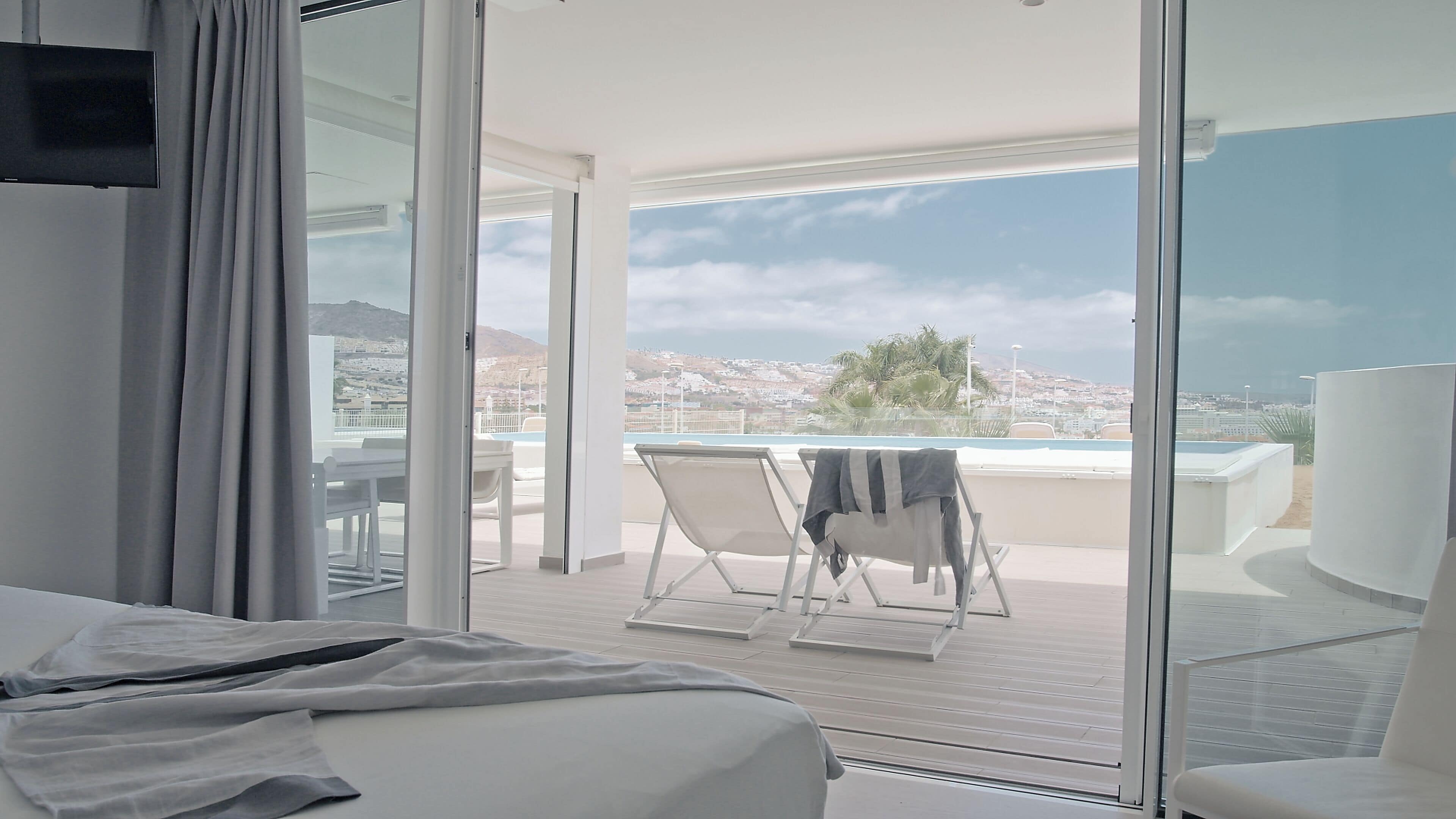 A hotel room with a large sliding glass door leading to a balcony with a pool and a view of a coastal town.