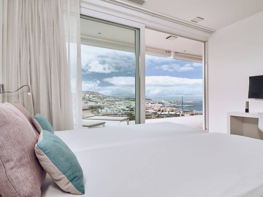 A modern hotel room with a large bed, a desk, and a TV. The room has a city view.