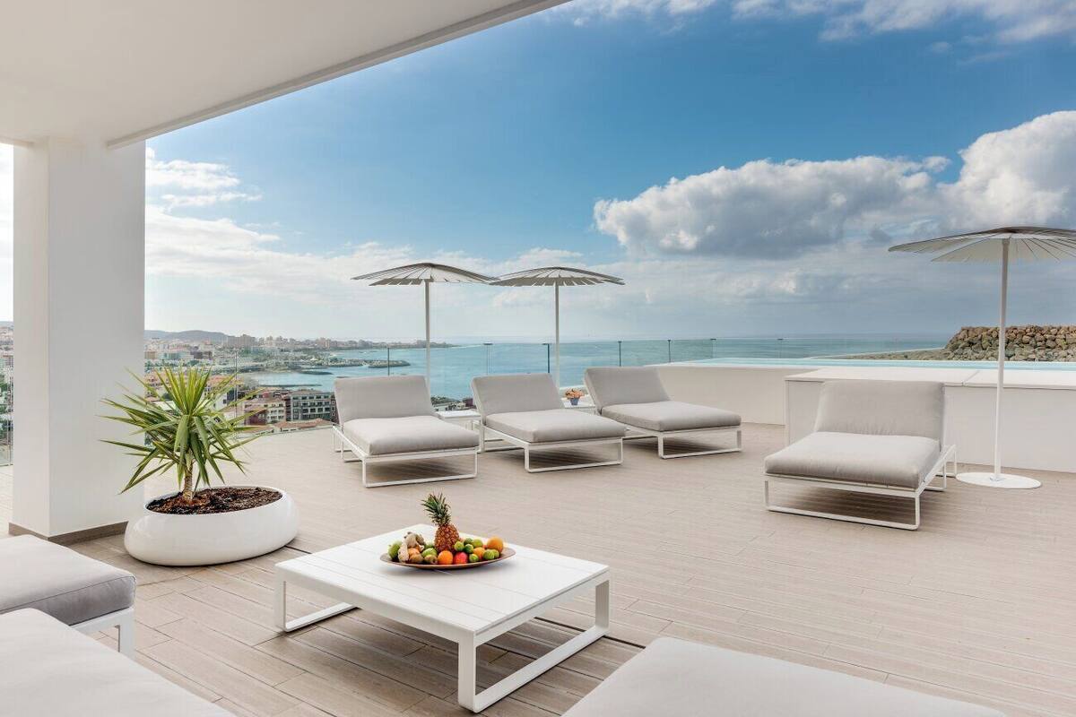 A rooftop terrace with white furniture, a potted plant, and a fruit bowl.