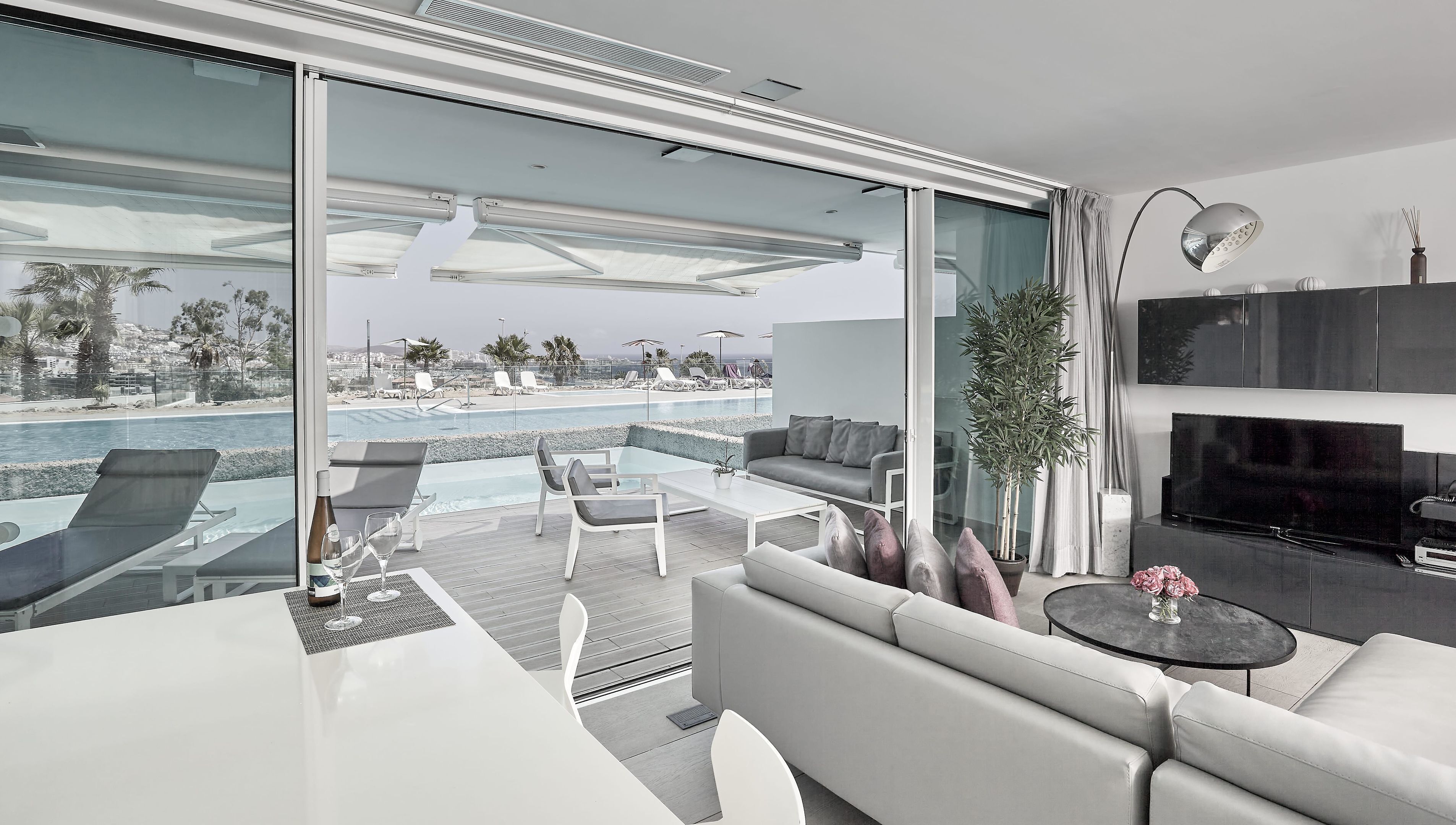 A modern living room with a glass wall overlooking a pool and cityscape.