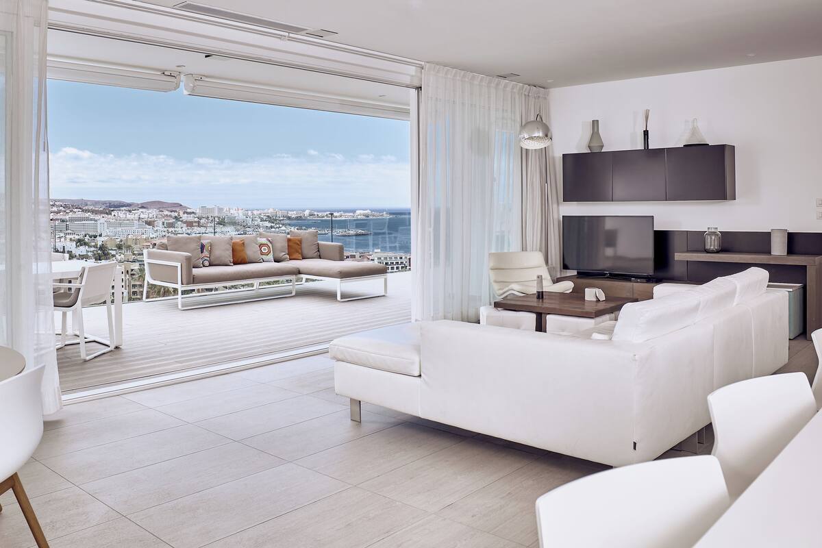 A modern living room with a sofa, a TV, and a dining area with a table and chairs.
