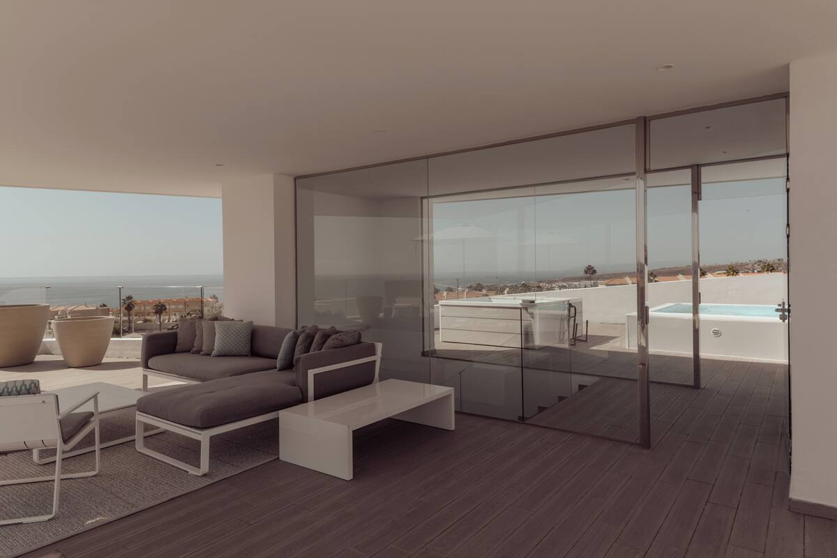 A modern living room with a sofa, coffee table, and large windows overlooking a pool and beach.