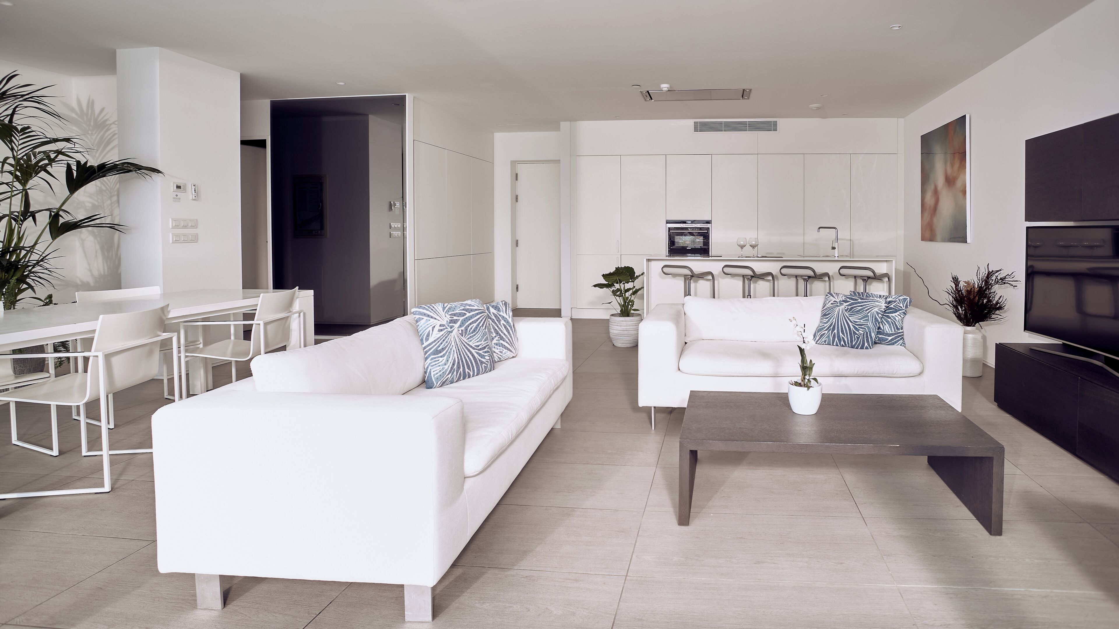 Una sala de estar moderna con sofás blancos, una mesa de centro y una zona de comedor con una mesa y sillas blancas.