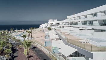 Un hotel moderno con varios balcones con vistas a una playa y al mar.