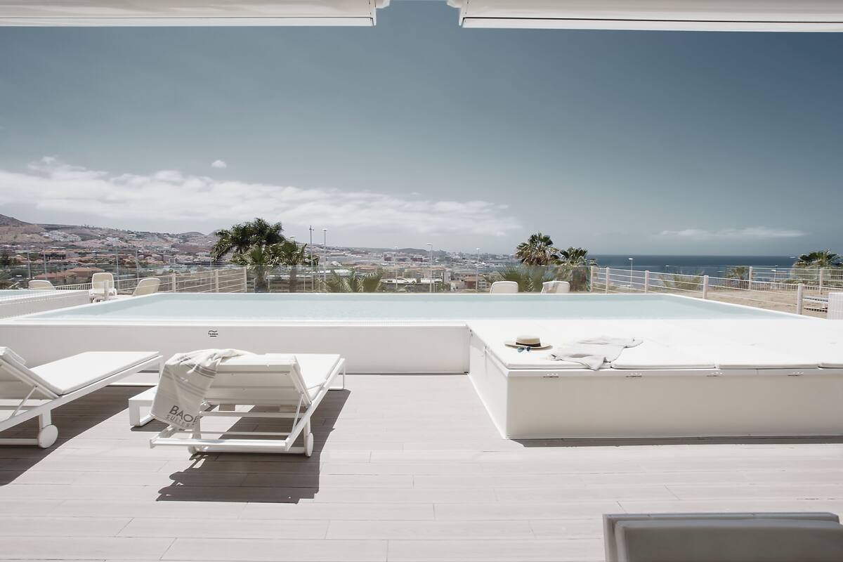 A rooftop infinity pool with white lounge chairs and a view of the city and ocean.